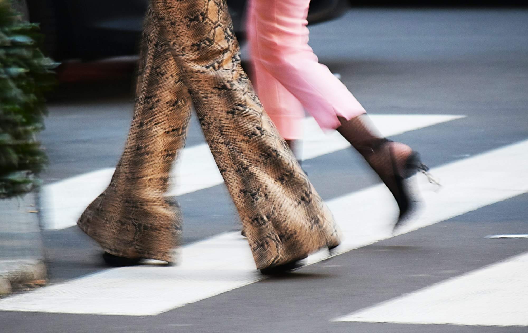 Wide snake-print trousers and pink tailoring crossing a Milan street