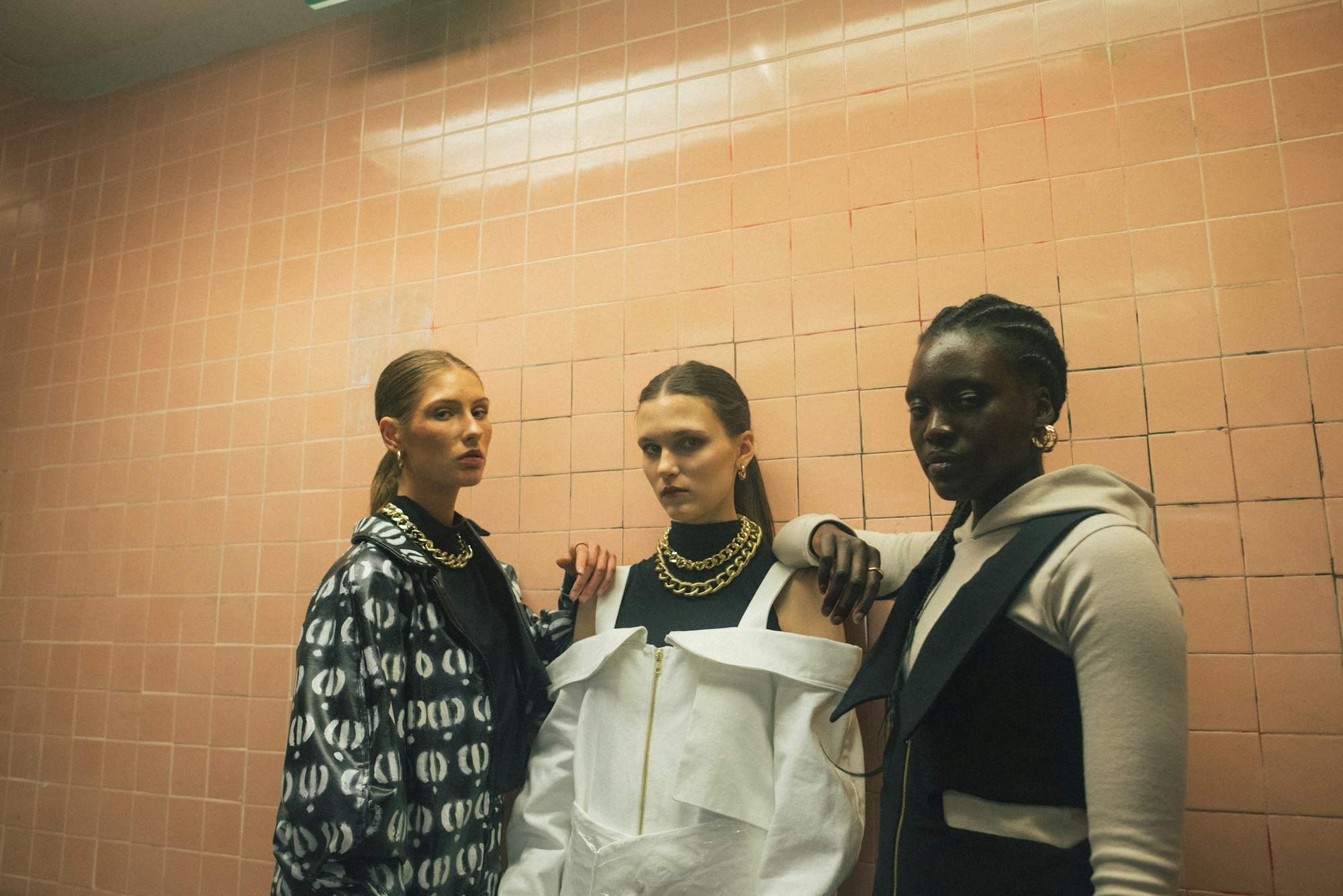 Three women in printed and tailored jackets against a pink tiled wall